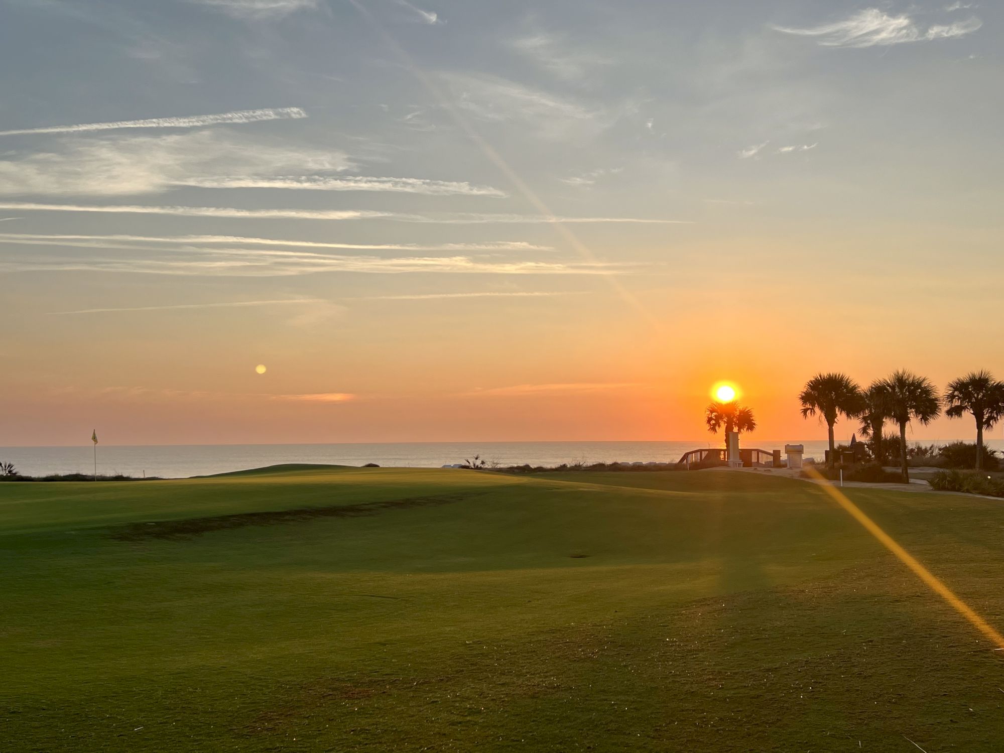 A peaceful sunrise over a golf course with palm trees and a clear sky in the background.