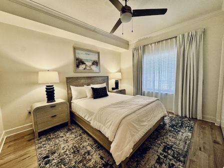 Cozy modern bedroom with a king bed, two nightstands, lamps, a ceiling fan, neutral decor, and a textured area rug by the window.