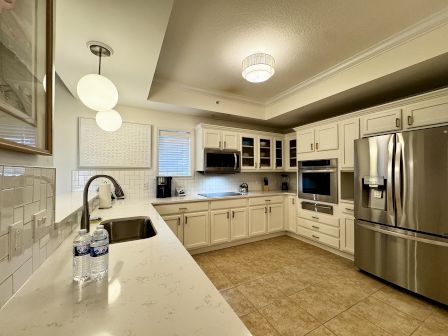A modern U-shaped kitchen with white cabinets, stainless steel appliances, a center island, tile floor, and bright pendant lights, neat and airy.