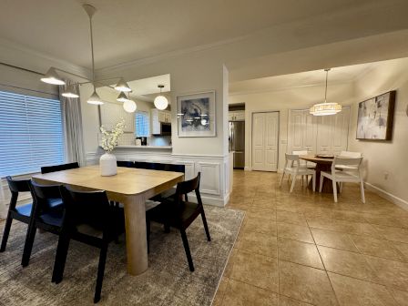 A modern open-concept dining area with a wooden table and six chairs, tile floors, pendant lights, a rug, and a separate cozy seating nook in the background.