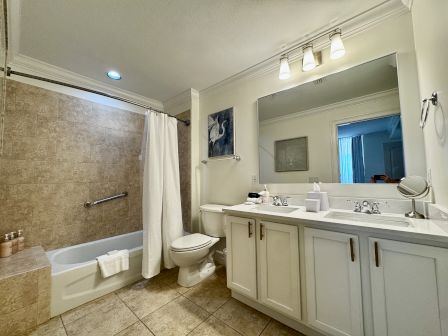 A clean bathroom with a bathtub/shower combo, beige tile, white toilet, double-sink vanity, and a large mirror, well-lit and modern.