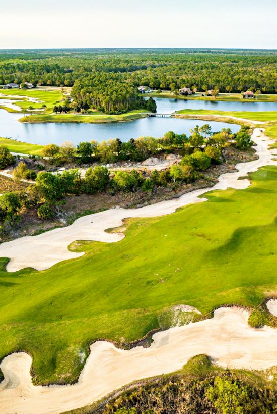 Aerial view of a sunlit golf course with green fairways, sand traps, and water hazards winding through a lush landscape, serene and expansive.