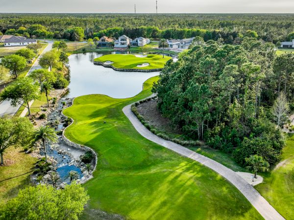 Aerial view of a lush golf course with winding fairways, water hazards, sand traps, and surrounding trees and buildings, peaceful and sunny.