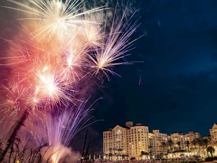 Fireworks illuminate the night sky above a large building complex, creating a vibrant display against the dark background.