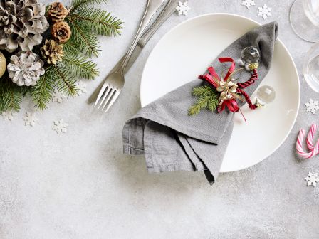 A festive table setting with a white plate, gray napkin tied with a ribbon and pine sprig, candy canes, snowflakes, and holiday garlands.