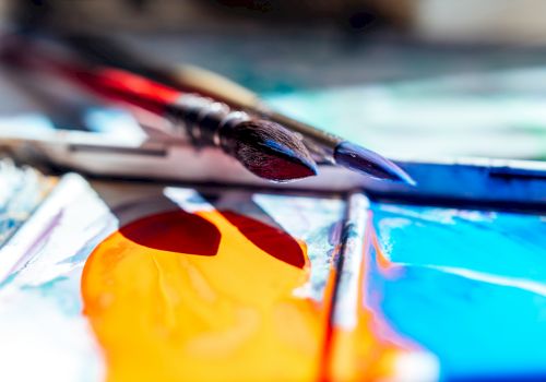 Paintbrushes and bright colors on a palette, ready for a watercolor session; vibrant oranges, blues, and reds ignite the canvas.