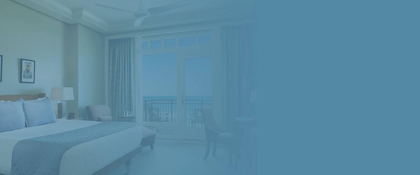 The image shows a hotel room with a bed, a lamp, a ceiling fan, and a view of the sea through balcony doors.