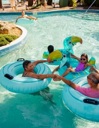 A group of people is floating on bright blue inflatable tubes shaped like ducks in a lazy pool ride, enjoying a sunny day.
