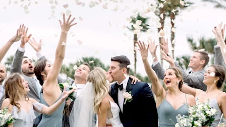 A wedding celebration with wedding party tossing petals, joy, and smiles as the bride and groom share a kiss surrounded by friends.