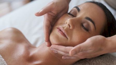 A woman receiving a relaxing facial massage with gentle, soothing hand movements on her neck and jawline.