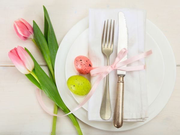 A pale table setting with a white plate, pink and green macarons, pink tulips, and cutlery wrapped with a pink ribbon on a napkin.