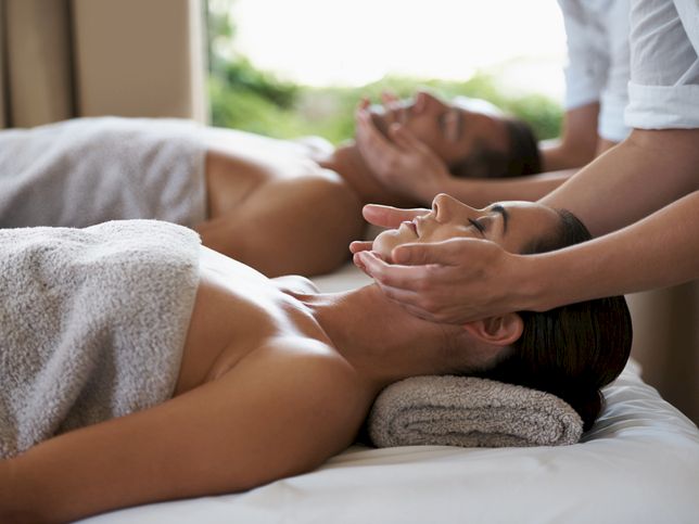 Two people receiving a spa-like face and neck massage, lying on massage tables with towels, peaceful and relaxing.