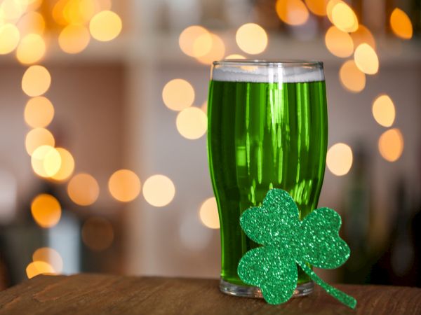 A green beer in a glass with a sparkly shamrock, set against bokeh lights for a festive St. Patrick's Day vibe.