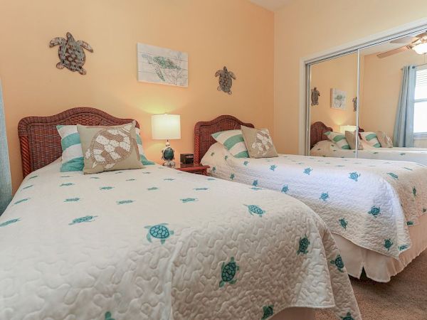 A bedroom with two twin beds, turtle-themed bedding, wicker headboards, and mirrored closet doors. Wall decor includes turtle art.