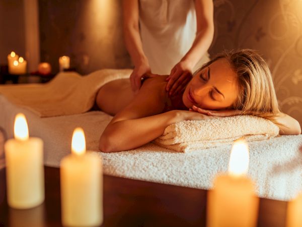 A woman gets a relaxing back massage in a dim, candlelit spa setting with warm, soothing ambiance.