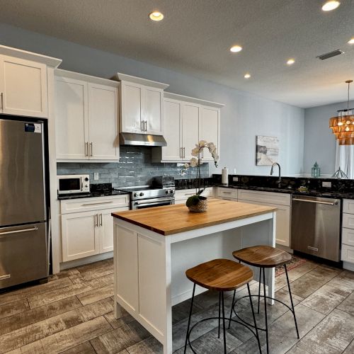 A modern kitchen with a central island, stainless steel fridge, dark cabinets, and pendant lights; bright and open with wooden floors.
