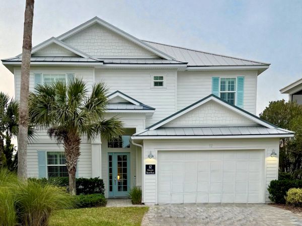 A two-story coastal-style house with a white exterior, gray roof, palm tree, manicured lawn, and a double garage. End.