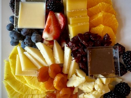 Assorted cheeses, berries, fruits, and dark chocolate squares arranged on a platter.