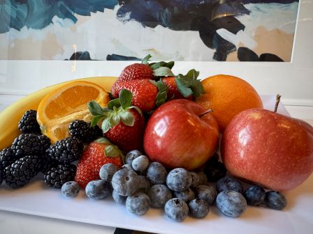 A colorful fruit plate featuring apples, oranges, strawberries, blueberries, blackberries, and orange slices arranged on a white surface.