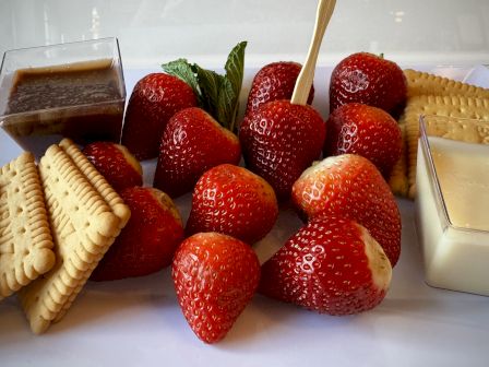 A platter of fresh strawberries with assorted dips: chocolate, cream, and cookies/crackers on the side, inviting and colorful.