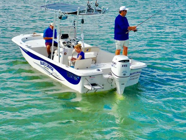 A small boat fishing on clear turquoise water, sunny skies, two anglers casting lines near a sandy shoreline.
