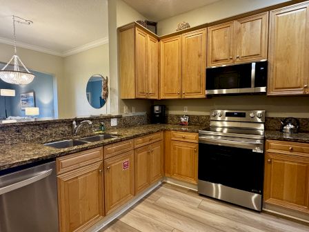 A modern L-shaped kitchen with wooden cabinets, granite countertops, stainless steel appliances, and a tile/wood floor ending in a bright dining area.