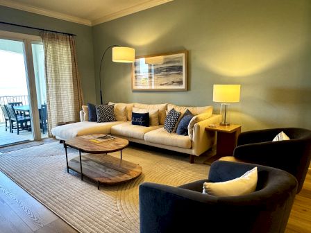 A bright living room with a beige sofa, blue cushions, two matching lamps, a round coffee table, armchairs, and a balcony door. Top it at 140 characters, always ending the sentence.