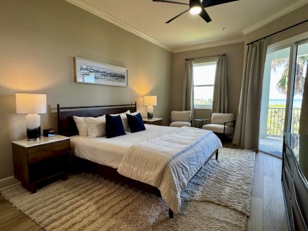 A luxurious hotel bedroom with a king bed, nightstands, soft lighting, a balcony view, neutral tones, and a cozy seating area.