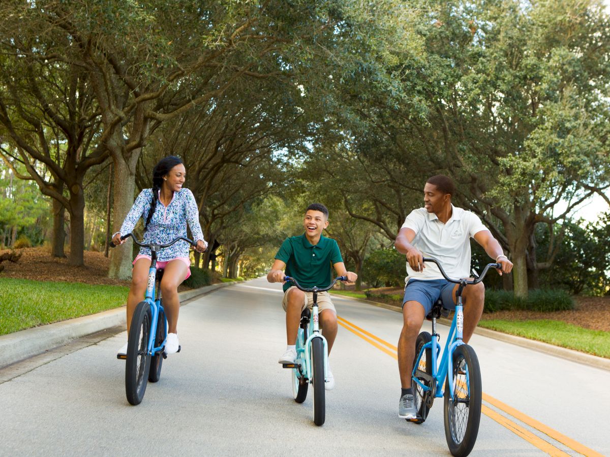 Three friends ride bikes on a sunny street, chatting and enjoying a playful moment together as they pedal side by side.