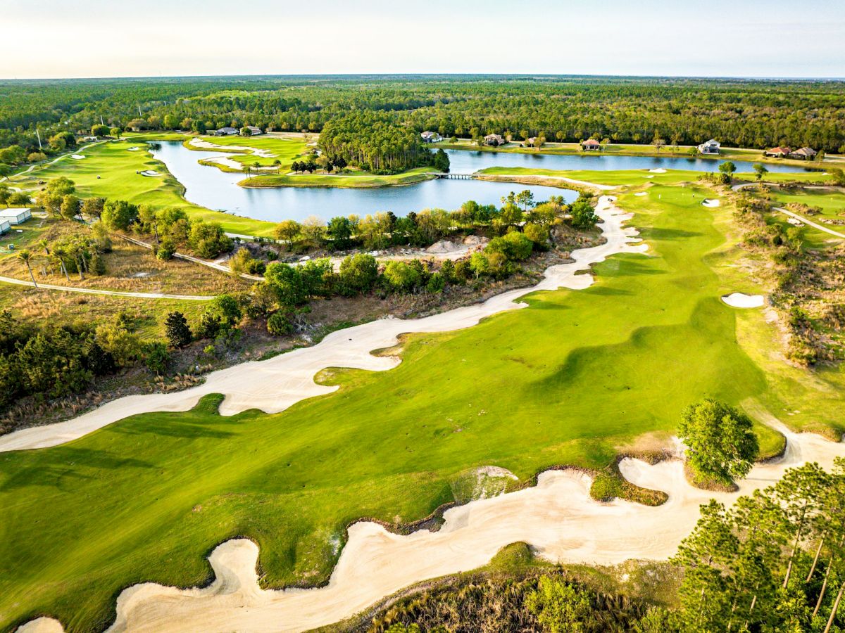 An aerial view of a lush golf course with bright green fairways, winding sand traps, and small water hazards, nestled among trees and open spaces.