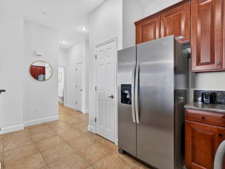 A bright home kitchen with tiled floor, wooden cabinets, a stainless refrigerator, and a small coffee/espresso setup on the counter.
