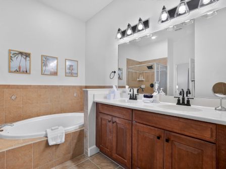 Bright bathroom with a bathtub, double vanity sinks, large mirror, glass shower, and ceiling track lighting above.