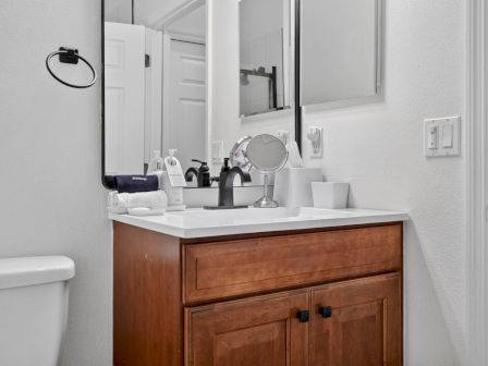 A bright bathroom with a white sink vanity, mirror, soap dispensers, towels, and a wall-mounted soap/toilet setup.