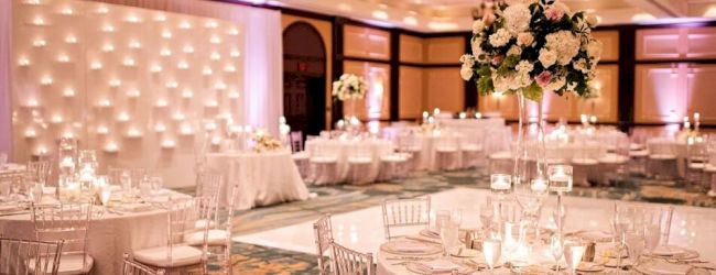 An elegantly decorated banquet hall with round tables, floral centerpieces, and a backdrop of lights, creating a warm, inviting atmosphere.
