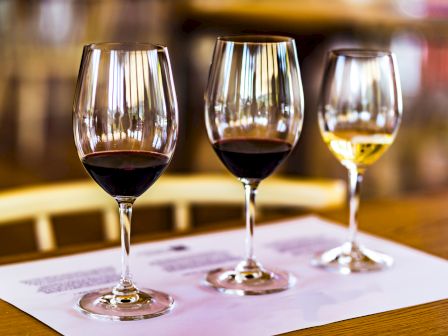 Three stemmed wine glasses on a table, filled with red and white wine, in a softly lit bar/restaurant setting.