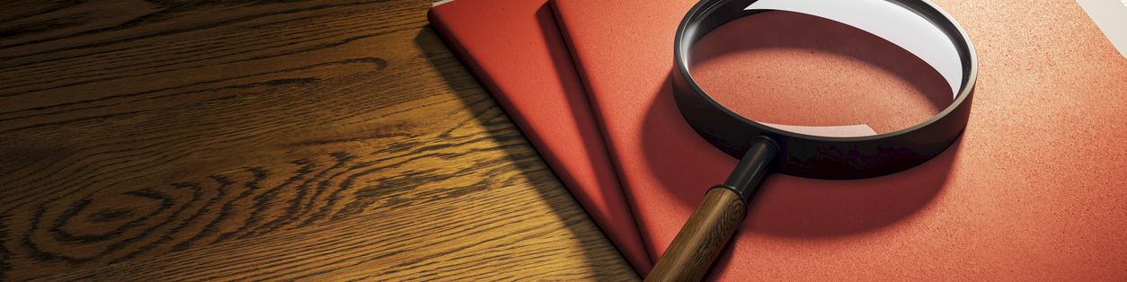 A magnifying glass and red books lie on a wooden table, suggesting research or investigation.