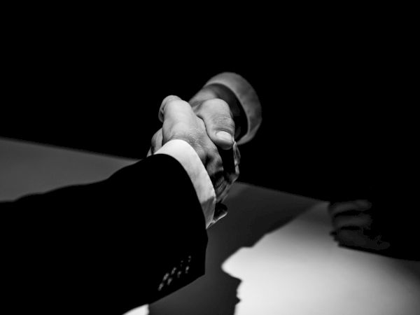 A black-and-white handshake between two people, shown against a dark background.