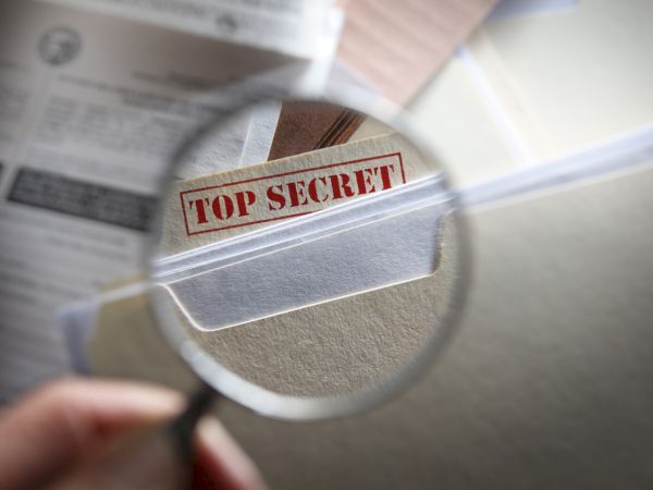 A magnified view shows a red &ldquo;TOP SECRET&rdquo; stamp over a document, suggesting classified information.