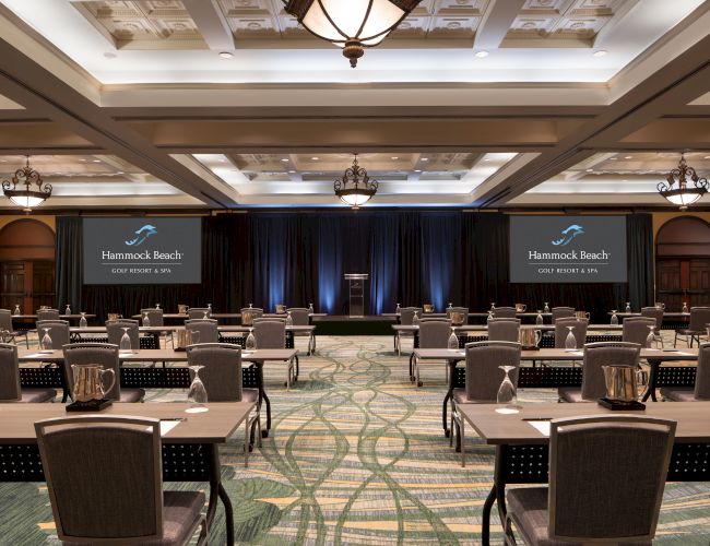 This image shows a conference room setup with tables, chairs, and screens displaying "Hammock Beach Golf Resort & Spa."