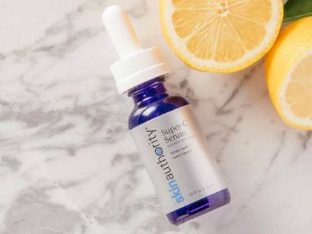 A small blue glass skincare serum bottle with a lemon slice on white marble, alongside another orange wedge for freshness.
