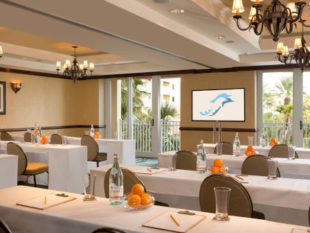A conference room set up with tables, papers, pencils, water bottles, and oranges, facing a screen with a dolphin logo.