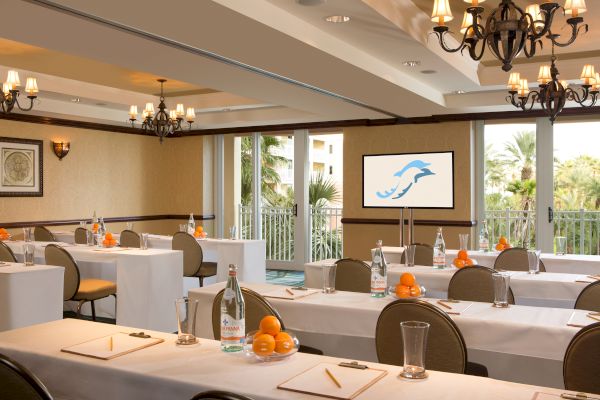 A conference room set up with tables, papers, pencils, water bottles, and oranges, facing a screen with a dolphin logo.