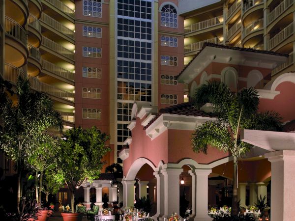 Outdoor courtyard of a hotel with tables, chairs, plants, and candles, surrounded by a multi-story building at dusk.