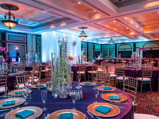 The image shows an elegant banquet hall setup with round tables, gold accents, and decorative centerpieces under warm lighting.