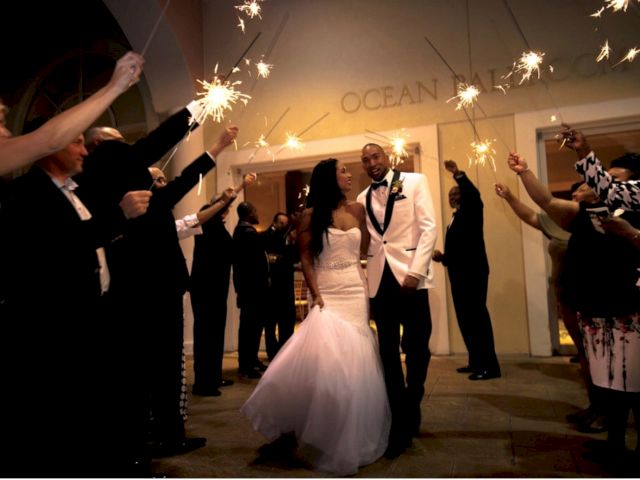 A bride and groom walk through guests holding sparklers, creating a celebratory archway at a wedding ceremony.