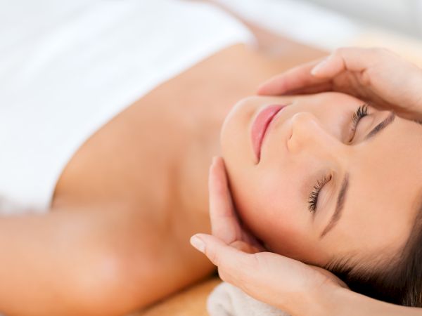 A person is receiving a facial massage, lying down with eyes closed, while hands gently cradle their face.