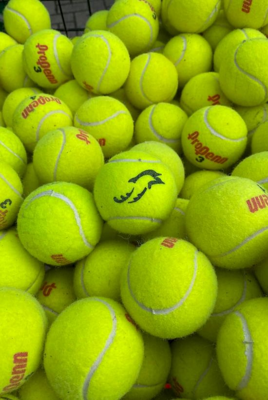 A pile of bright yellow tennis balls, some branded with "Wilson," and one ball features a different logo in black ink.