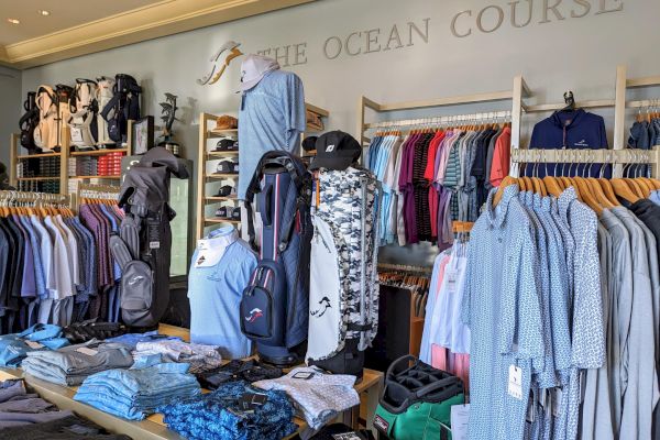 A golf shop with shirts, golf bags, and accessories on display, under the sign "The Ocean Course."