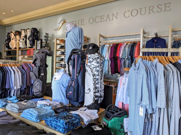 A golf shop with shirts, golf bags, and accessories on display, under the sign "The Ocean Course."
