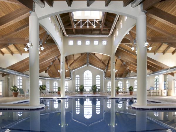 A spacious indoor swimming pool with vaulted wooden ceilings, elegant columns, and large windows letting in natural light.